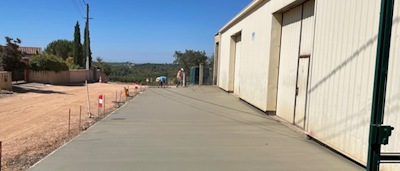 Photo de deux ouvriers en arrière plan en train de couler une dalle pour faire une terrasse devant un hangar