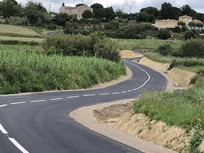 Photo d'une route avec des virages, des champs sur le bord de la route et des maisons dans le fond